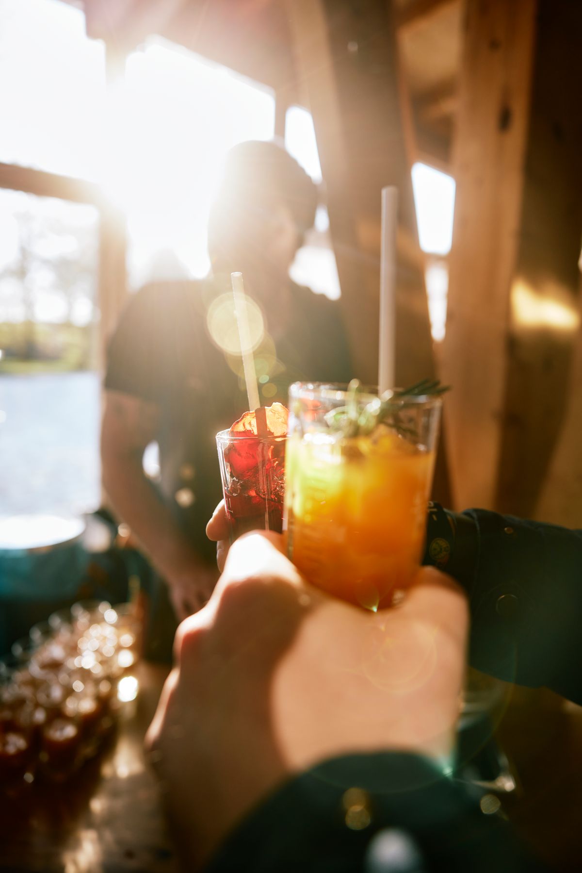 Zwei Cocktails werden im Gegenlicht über einer Bar angestoßen