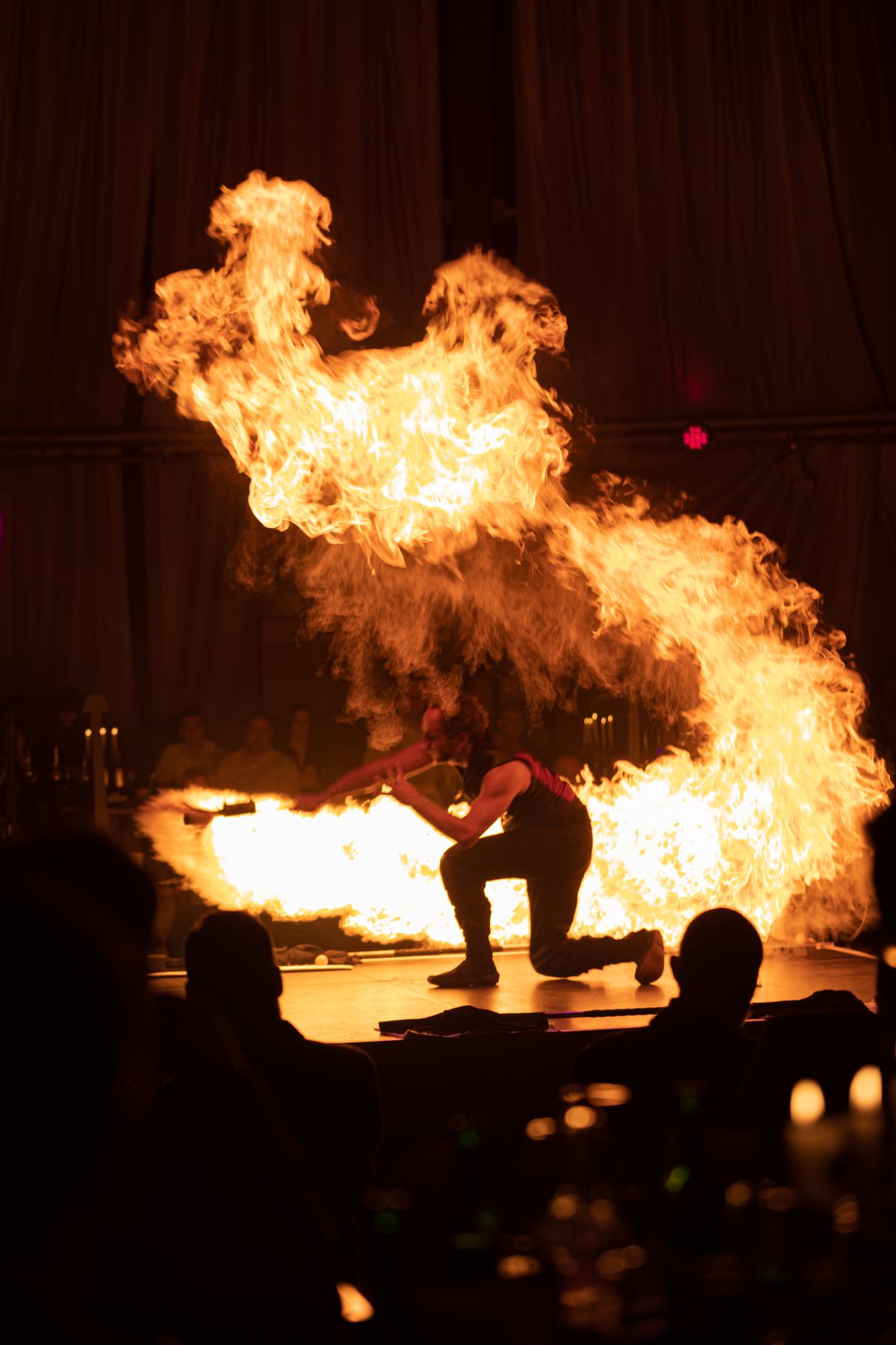 Feuerkünstler auf einer Bühne, eine große Flamme vor dunklem Saal mit Publikum